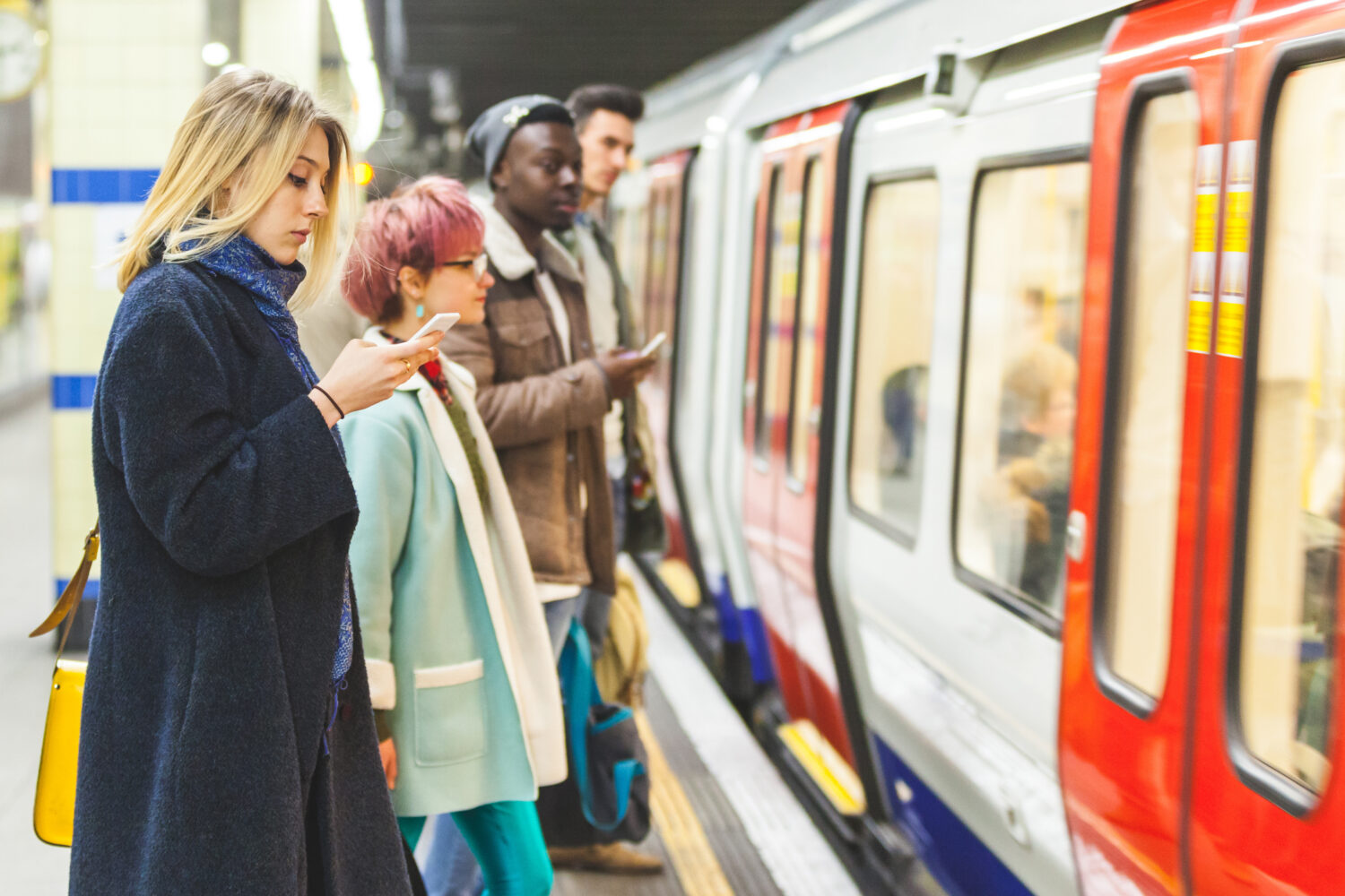 People waiting for the train at subway station. Mixed race persons, two men and two women, staying on a line and waiting to board the train. Commuting and transport