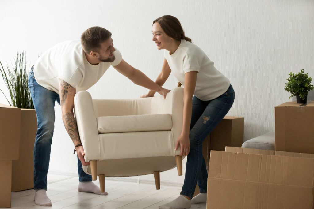 Young couple carrying chair together, house improvement, modern furniture in new home concept, man and woman moving into own flat after relocation furnishing living room, remodeling and renovation