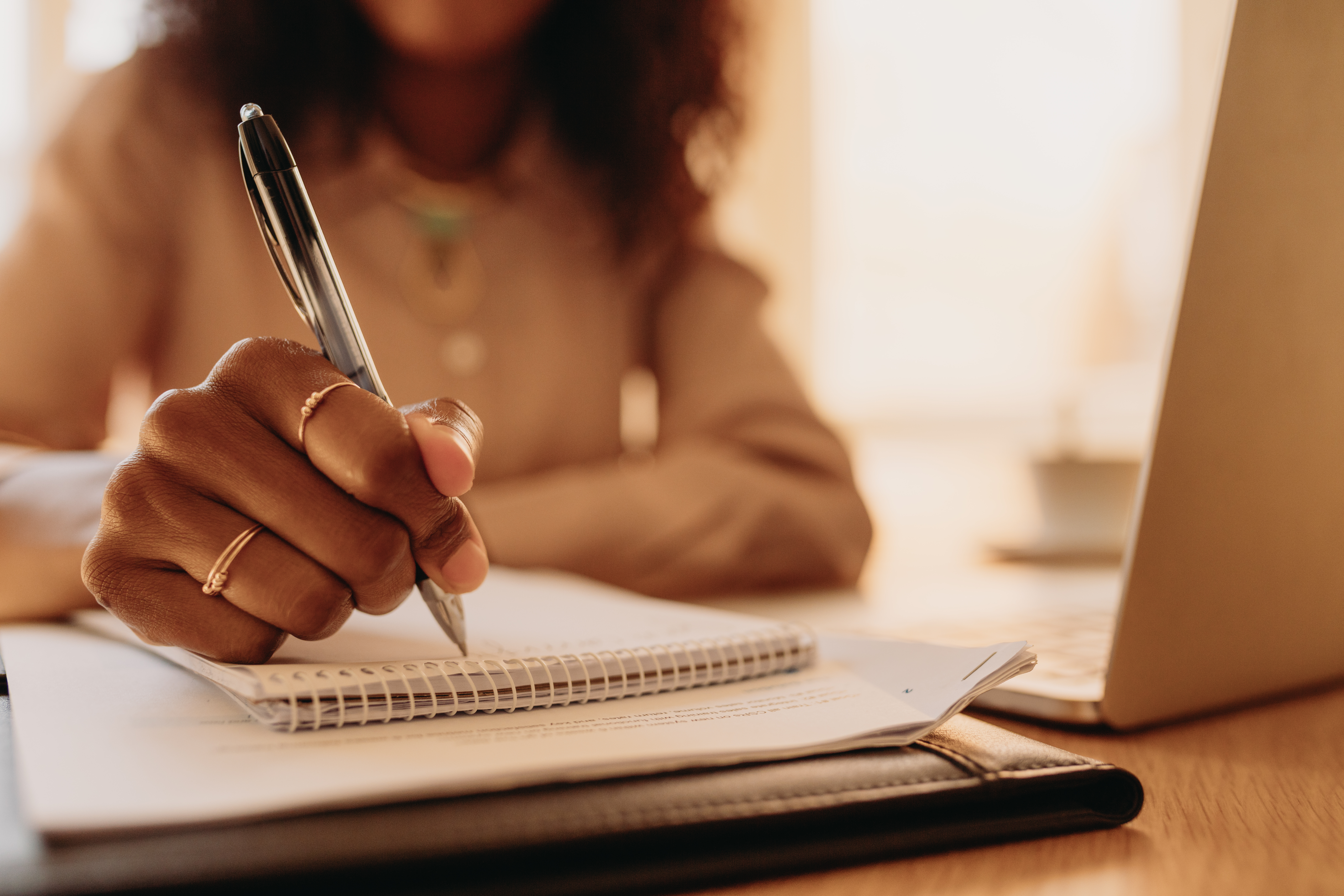 Businesswoman working on laptop computer sitting at home. Close up of hand of a woman holding pen and writing on notepad.