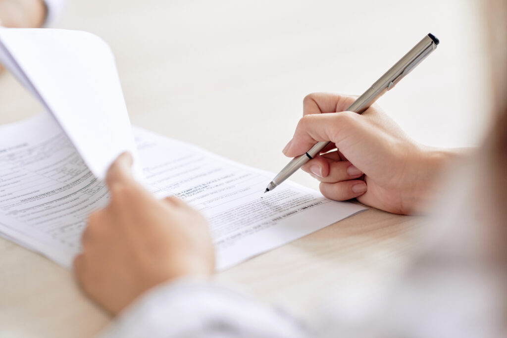 Crop shot of person with pen signing contract at desk in daylight