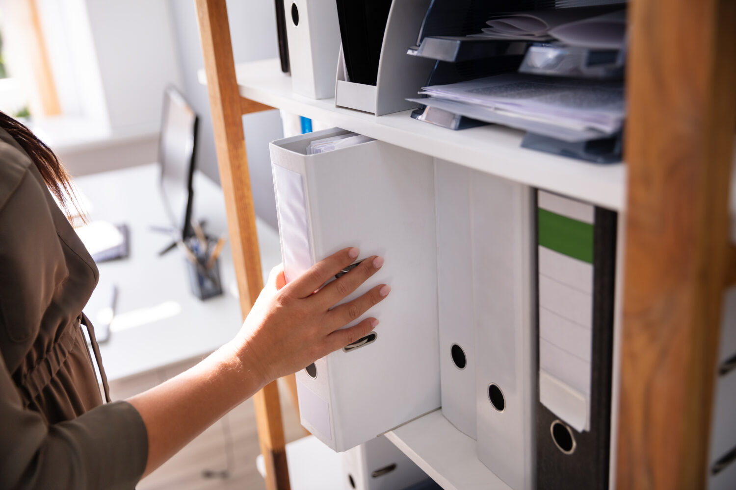 Businessperson's Hand Taking Folder From Wooden Shelf In Office