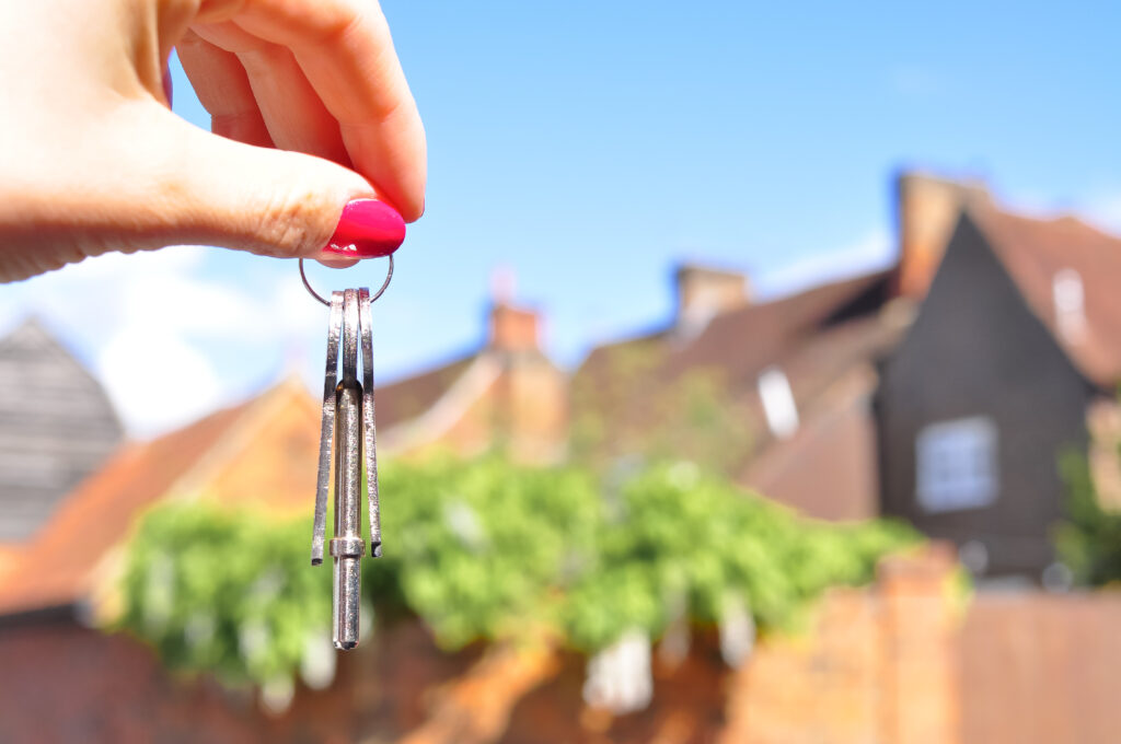 Woman's hand with metal keys on blurred background with house. High quality photo