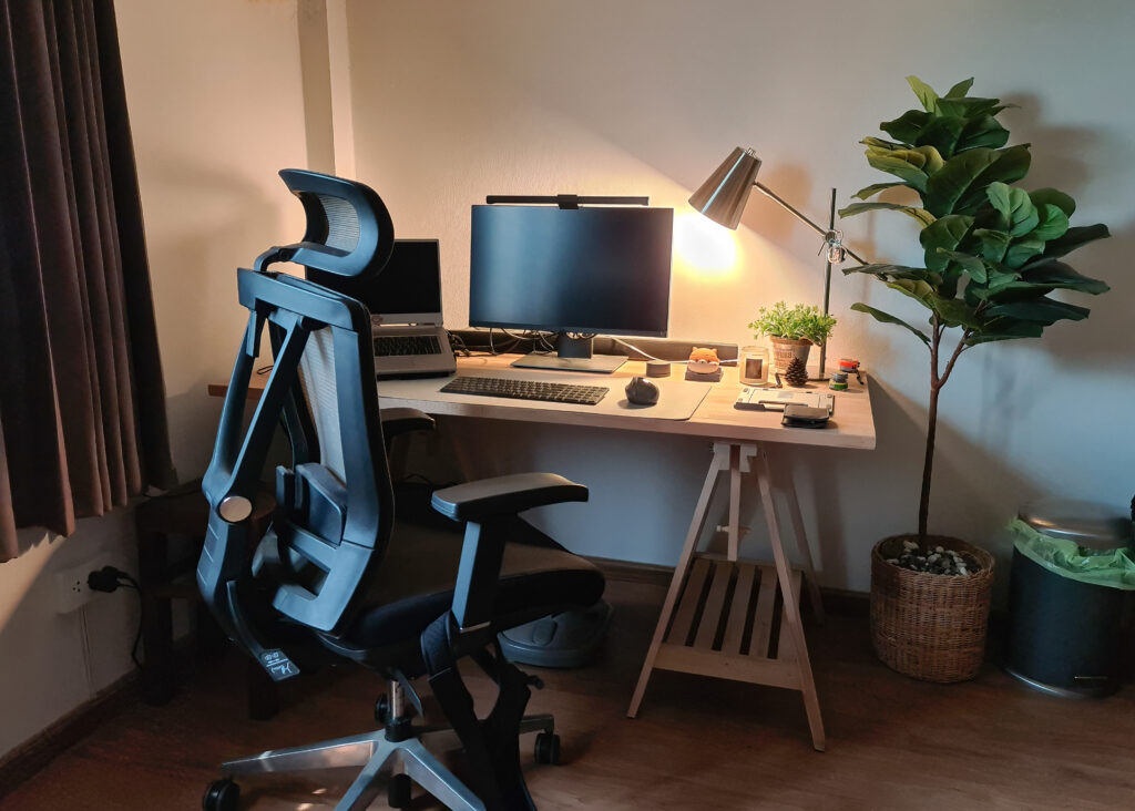 Working corner with monitor, laptop, wooden desk, ergonomic chair and decorate object in bedroom