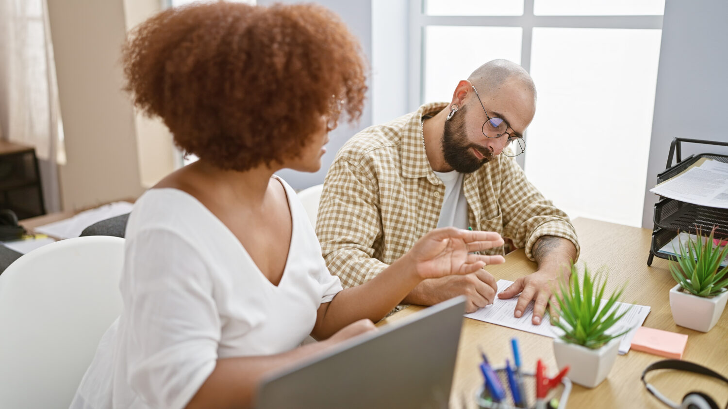 Two office workers, a man and woman, seriously concentrate on taking notes while working on a laptop