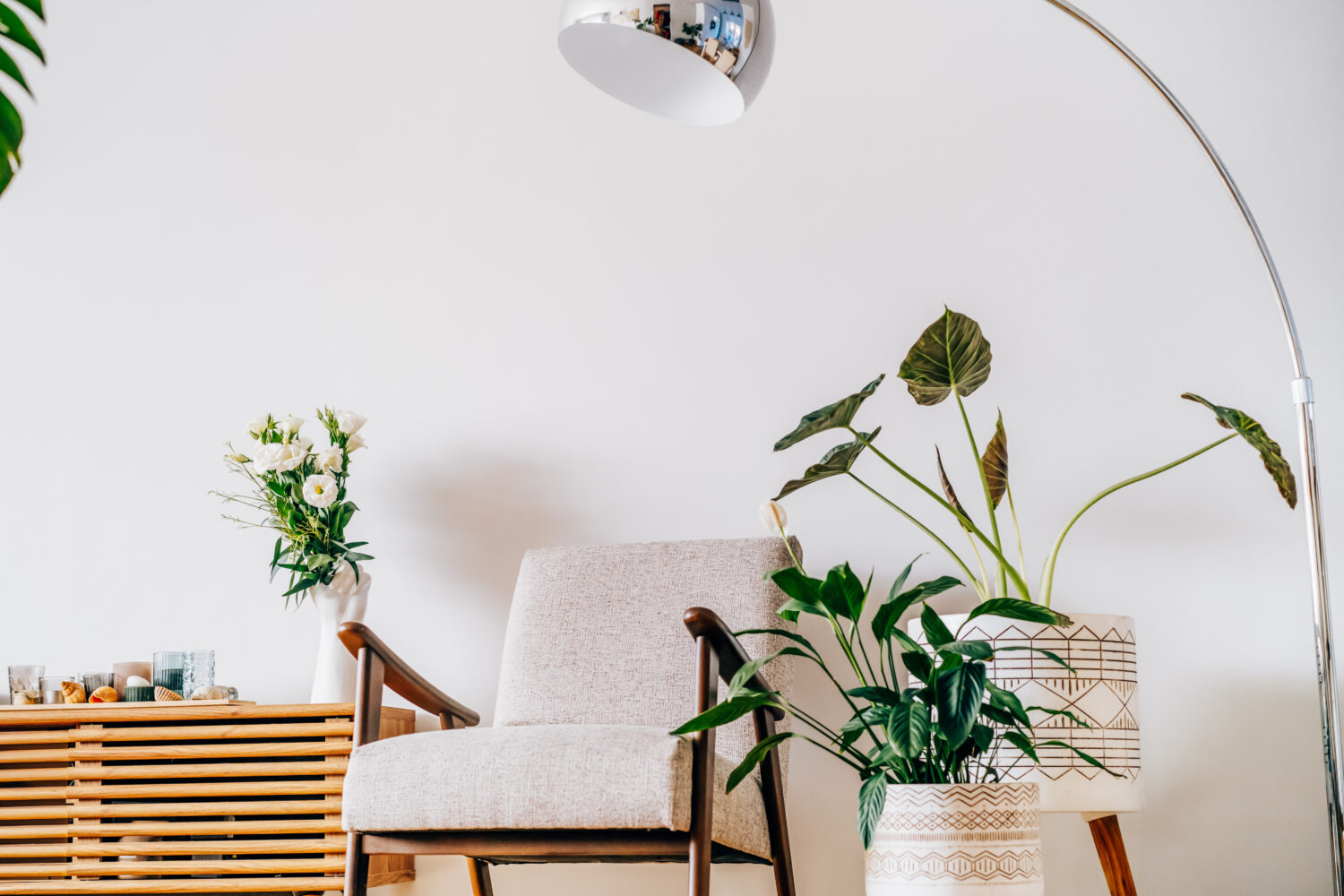 Stylish modern Scandinavian interior of living room with candles and fresh flowers on the wooden console, retro style armchair, floor lamp and potted green home plants. Cozy home interior design.