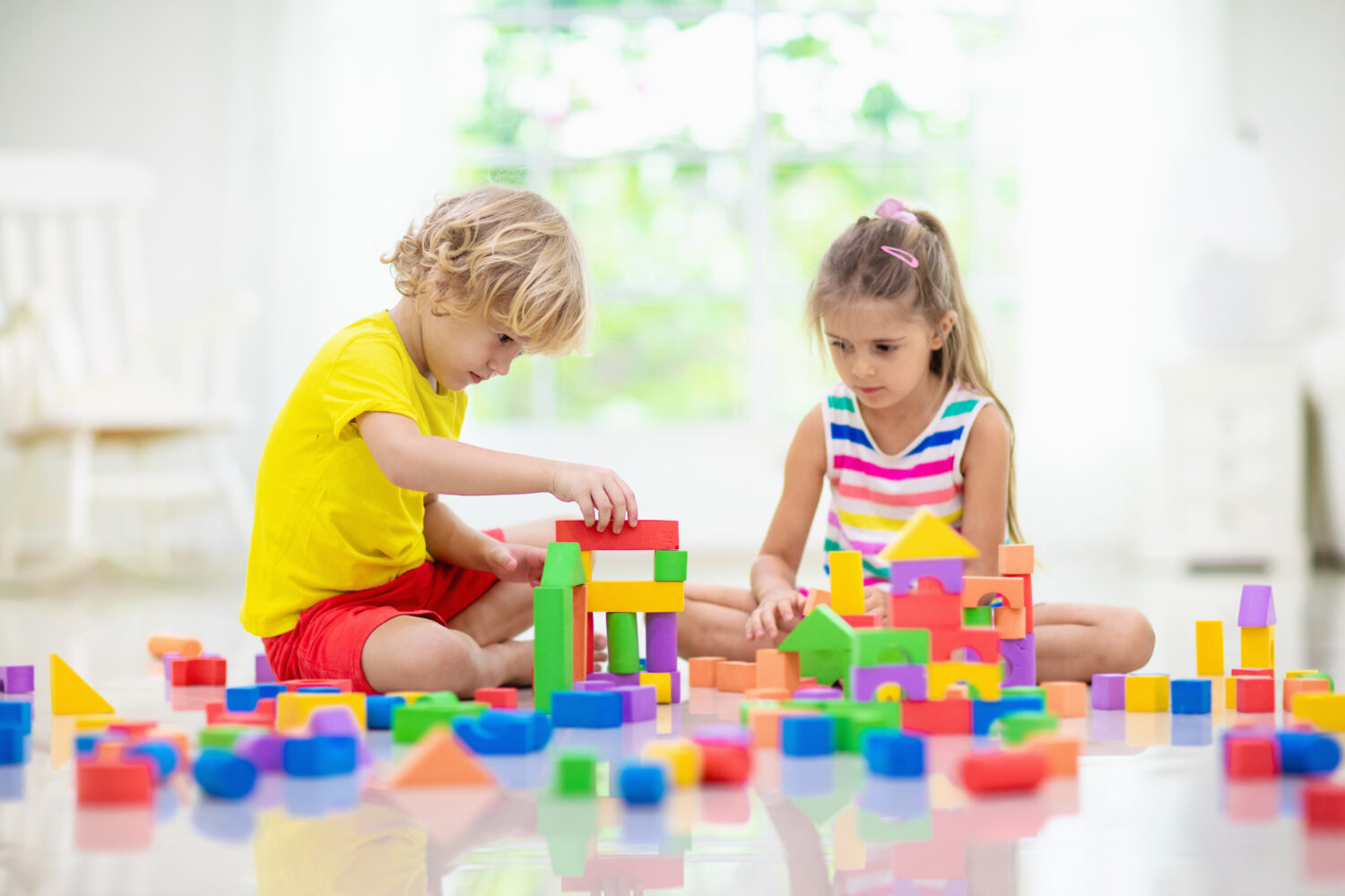 Kids play with colorful blocks. Little boy and girl build tower at home or day care. Educational toy for young child. Construction creative game for baby or toddler kid. Mess in kindergarten playroom.