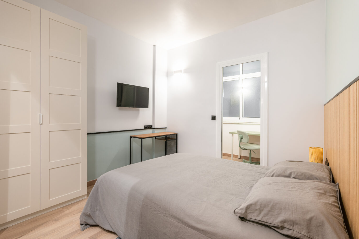 Small compact stylish bedroom in stylish soothing colors with double bed, TV, built-in wardrobe and table. Concept of small cozy bedroom or hotel room