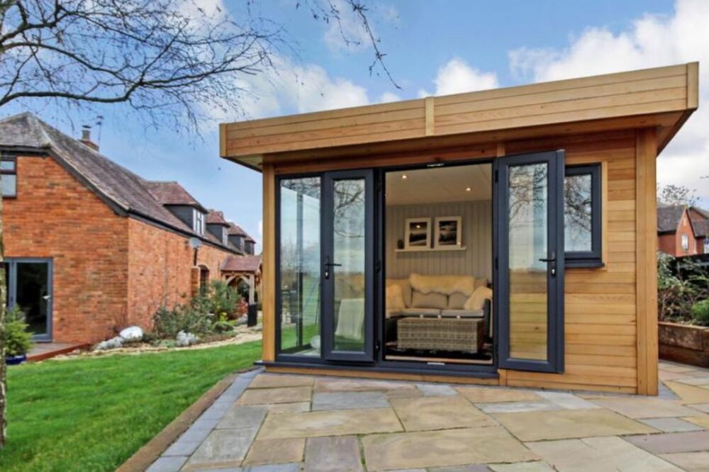 Contemporary Garden Office Nottingham - Cedar Garden Room Contemporary insulated garden office in Nottingham, featuring cedar cladding, modern black-framed glazing and a bright interior. Exterior view on pavement next to a house.