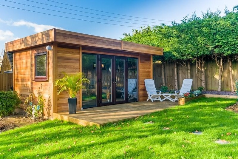 Contemporary Timber Garden Room with Decking and Bi-Fold Doors Contemporary timber garden room with large glazed doors and wooden decking in a lawn.