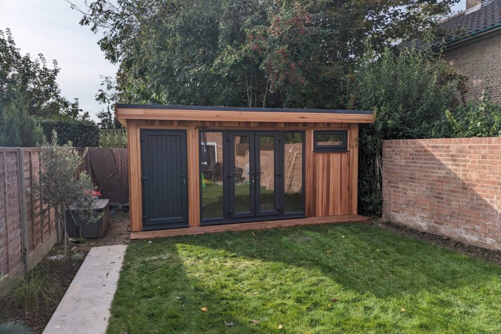 Contemporary timber garden room with black French doors, side storage, small window, and natural wood cladding in a garden.