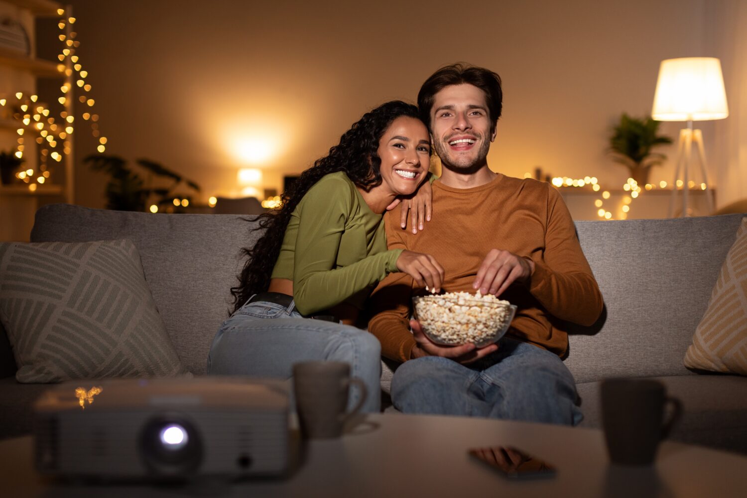 a couple sitting on a comfy couch, watching a movie while eating popcorn