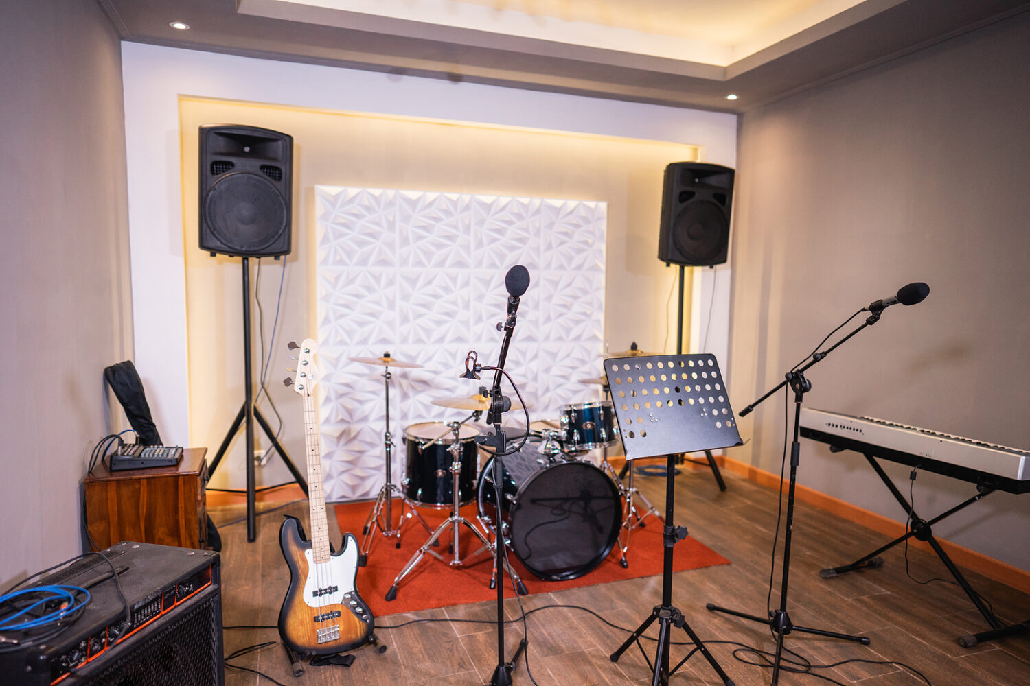 Modern music studio interior with a drum kit, bass guitar, keyboard, microphones, speakers and wall panels with lighting.