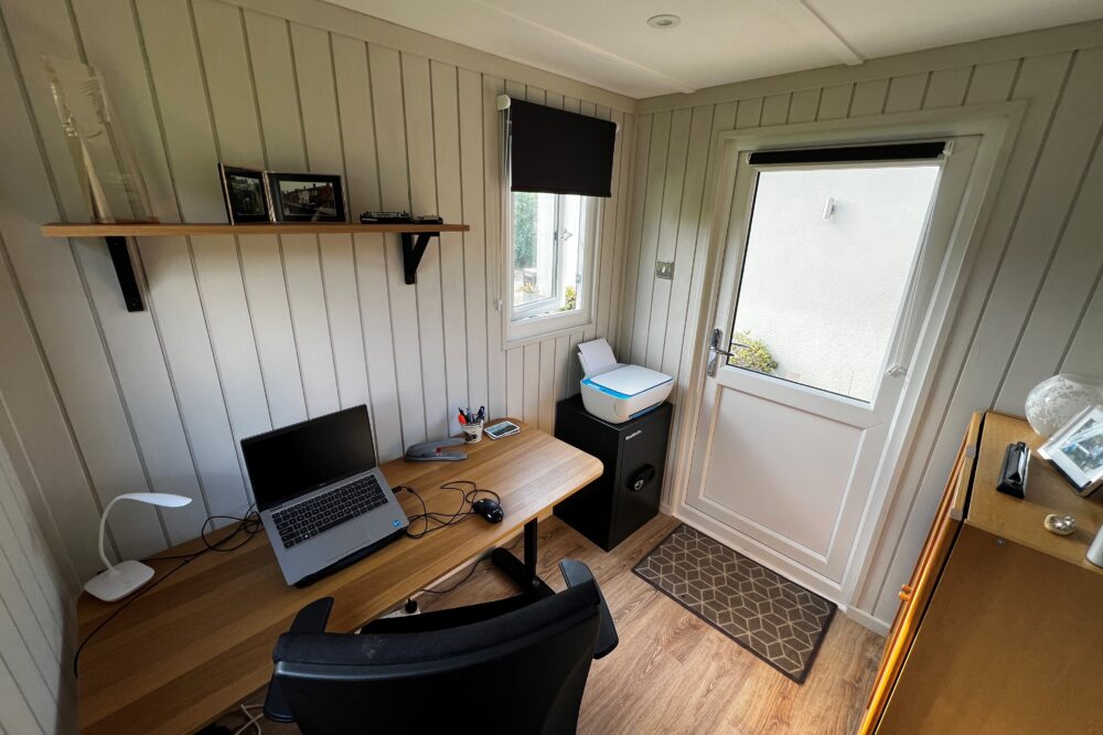 Micro Garden Office Pod Interior with Compact Home Workspace Modern garden office pod interior featuring a wooden desk, laptop, office chair, vertical timber wall panelling, shelving and a glazed entrance door.