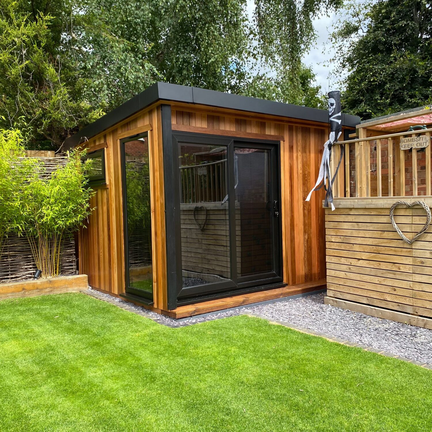 Exterior view of a modern cedar-clad micro office pod in the UK with black framed doors and windows in a landscaped garden.