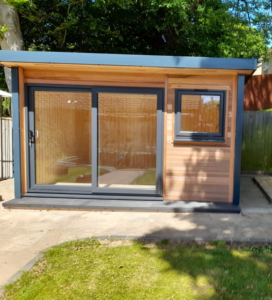 Modern timber garden office pod featuring natural wooden cladding, anthracite grey sliding glass doors, a matching window and a contemporary flat roof.
