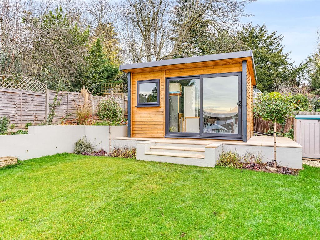 Modern timber garden office pod with sliding glass doors, black-framed window and steps overlooking a landscaped lawn.