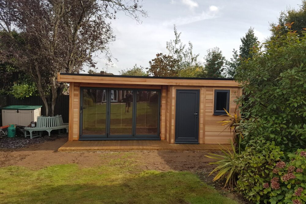 Modern timber garden office shed featuring natural wooden cladding, large anthracite grey glazed doors, a separate entrance, matching window and contemporary flat roof.