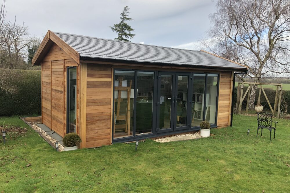 Modern timber garden studio featuring natural wooden cladding, anthracite grey sliding glass doors, a matching window and a contemporary flat roof in high Wycombe.