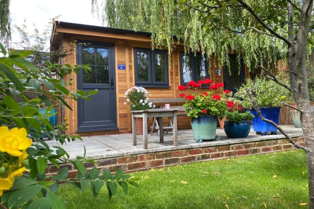Traditional Timber garden room with grey doors and windows surrounded by plants and flowers